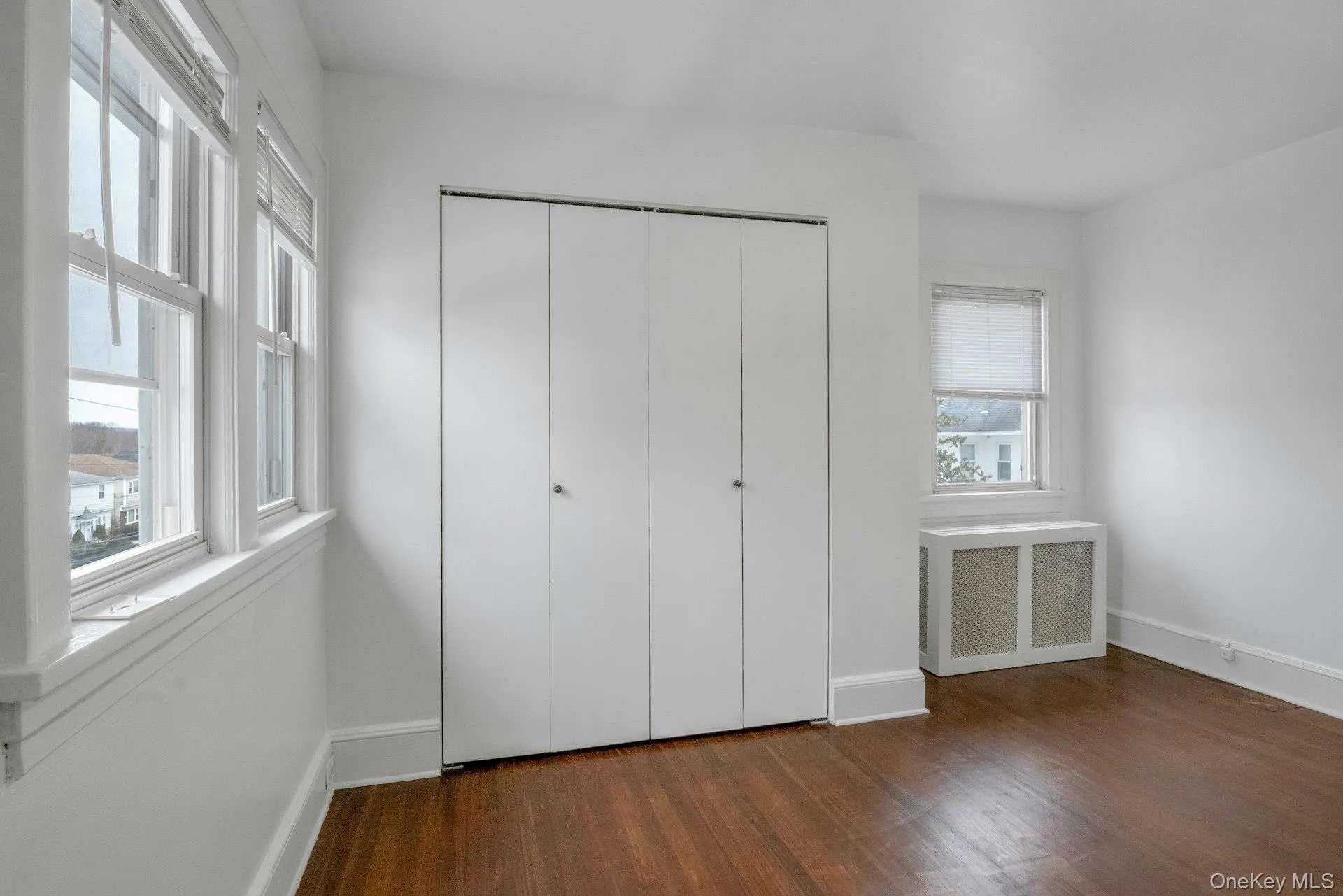 Unfurnished bedroom with radiator, dark wood finished floors, and a closet Unfurnished bedroom with radiator, dark wood finished floors, and a closet