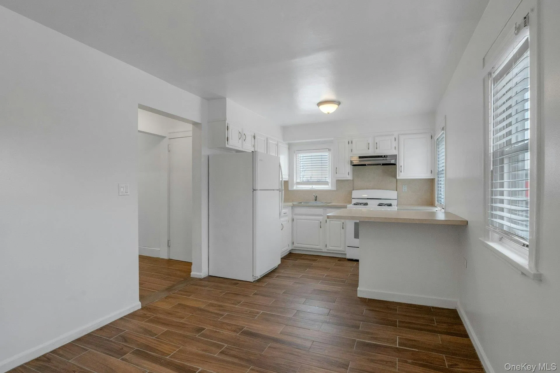 Kitchen with white appliances, white cabinets, light countertops, a peninsula, and wood tiled floors Kitchen with white appliances, white cabinets, light countertops, a peninsula, and wood tiled floors
