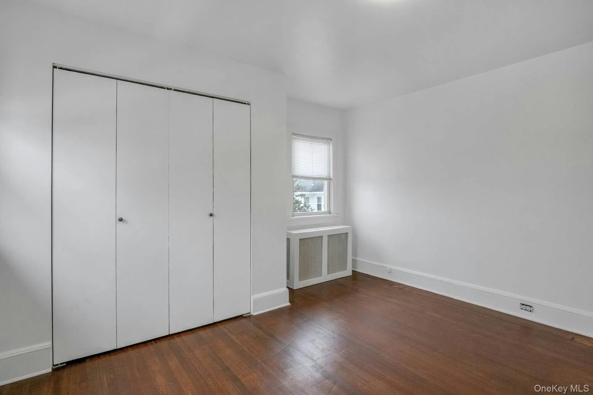 Unfurnished bedroom with radiator, dark wood-type flooring, and a closet Unfurnished bedroom with radiator, dark wood-type flooring, and a closet