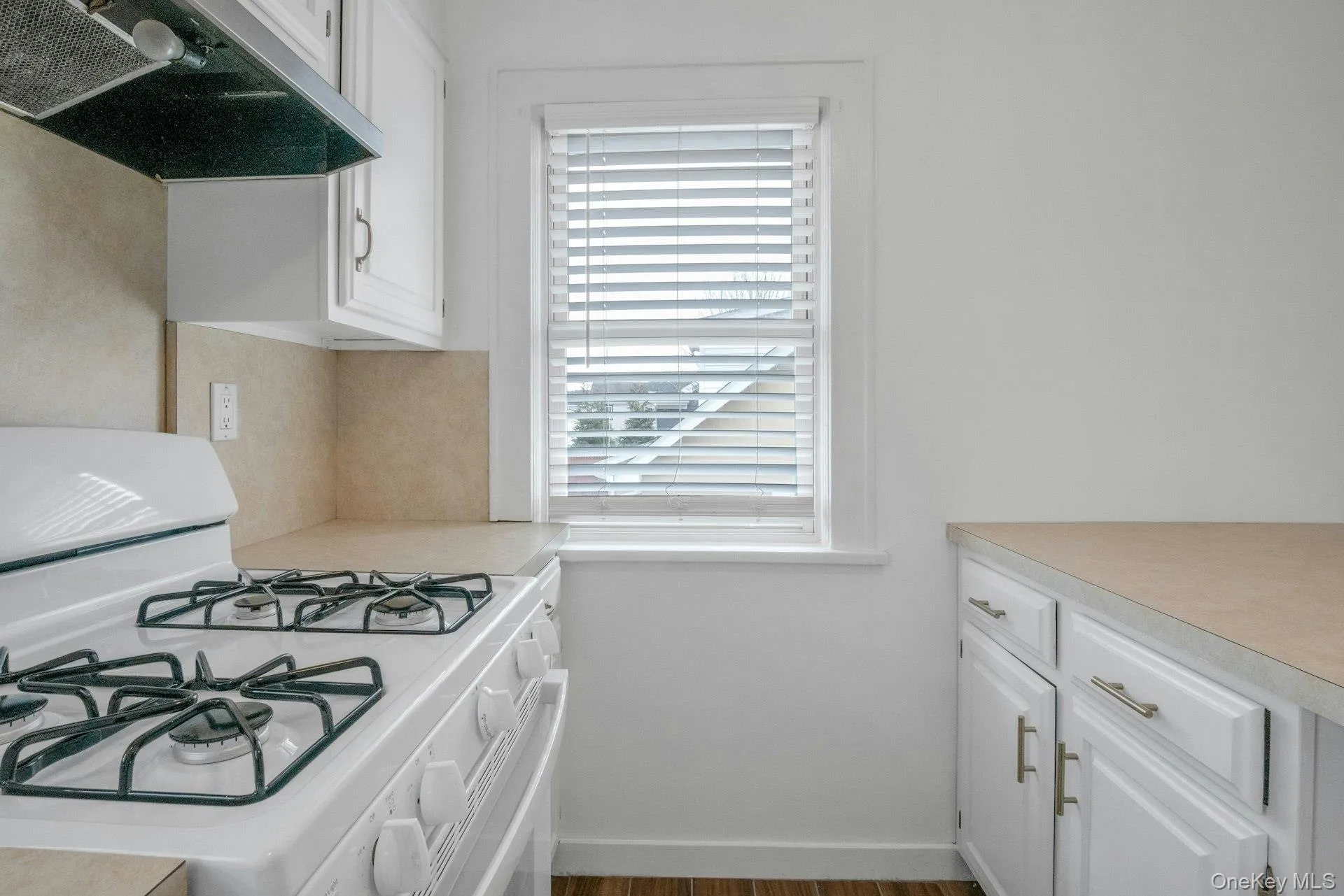Kitchen featuring white cabinetry, white gas stove, exhaust hood, light countertops, and wood finished floors Kitchen featuring white cabinetry, white gas stove, exhaust hood, light countertops, and wood finished floors