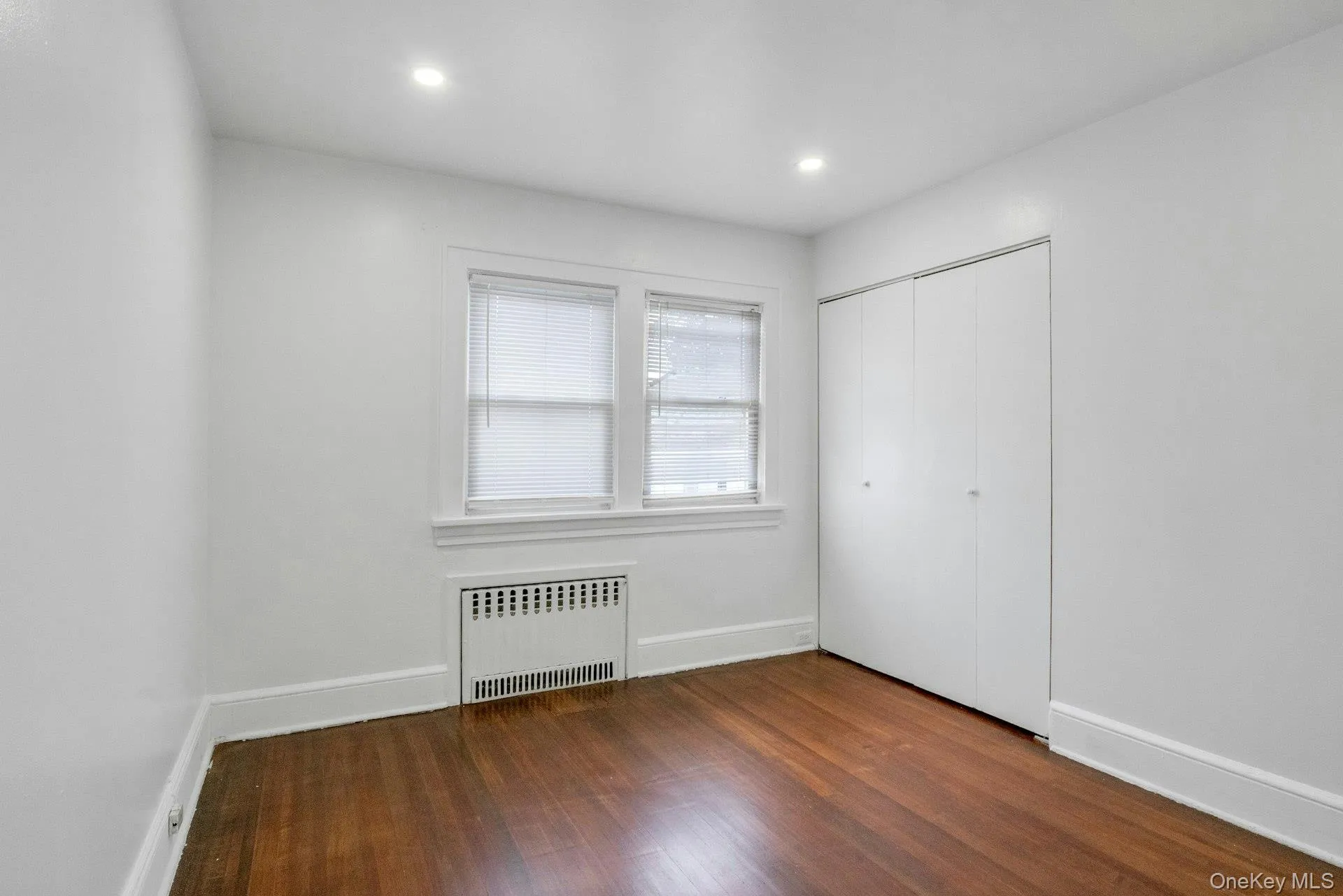 Unfurnished bedroom featuring radiator, dark wood-style floors, a closet, and recessed lighting Unfurnished bedroom featuring radiator, dark wood-style floors, a closet, and recessed lighting