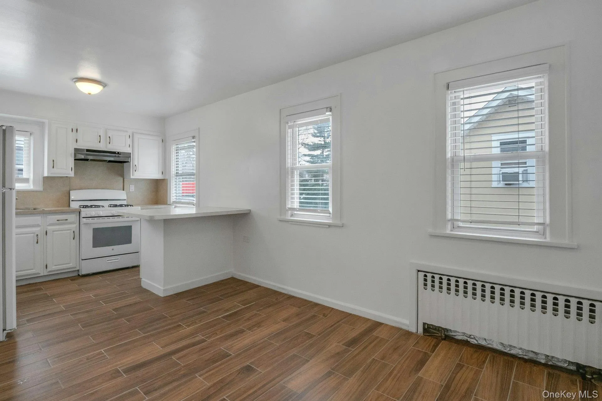 Kitchen featuring radiator heating unit, white cabinetry, light countertops, white appliances, and wood tiled floors Kitchen featuring radiator heating unit, white cabinetry, light countertops, white appliances, and wood tiled floors