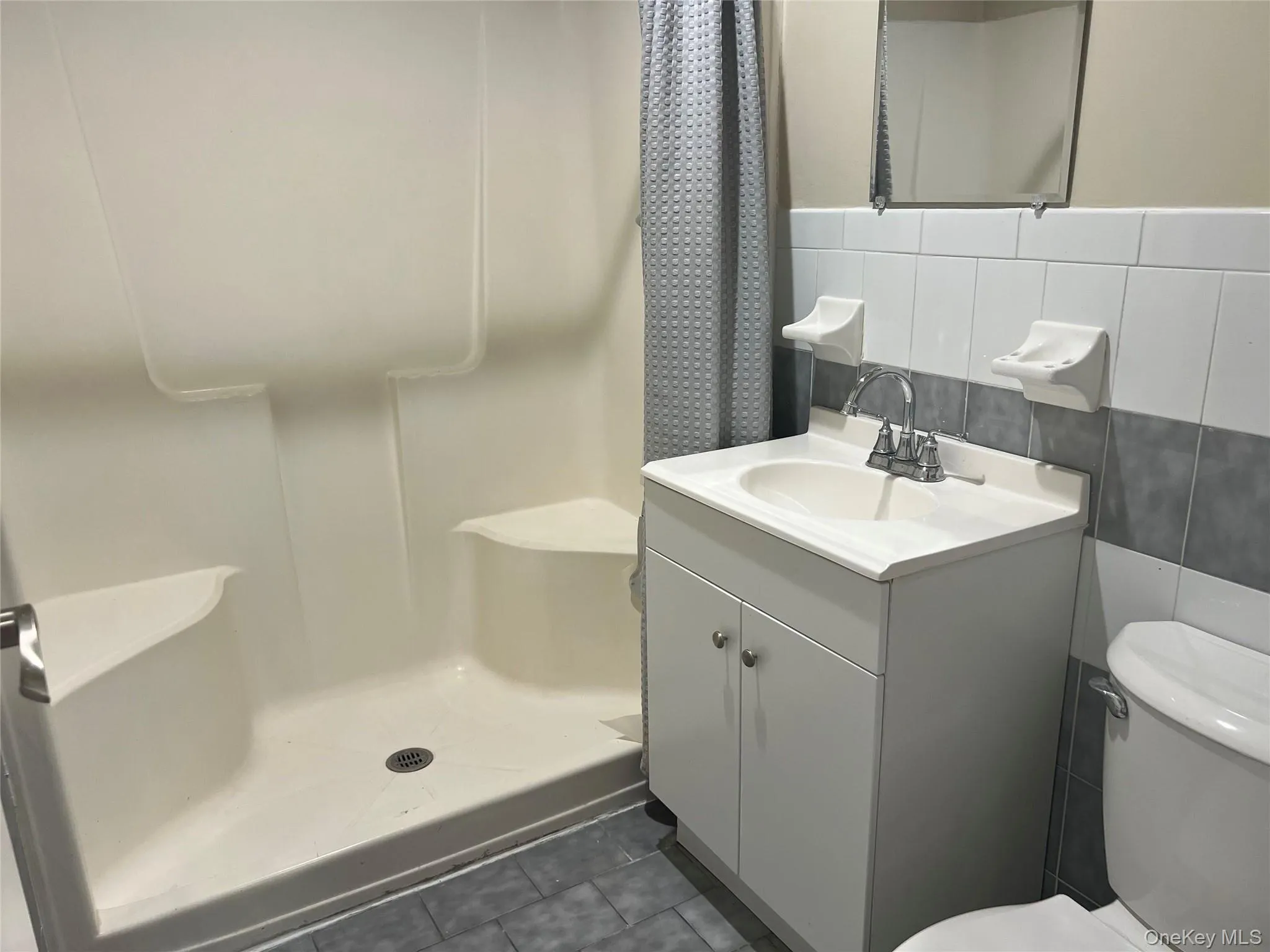 Full bathroom with a stall shower, tile walls, vanity, dark tile patterned flooring, and tasteful backsplash Full bathroom with a stall shower, tile walls, vanity, dark tile patterned flooring, and tasteful backsplash