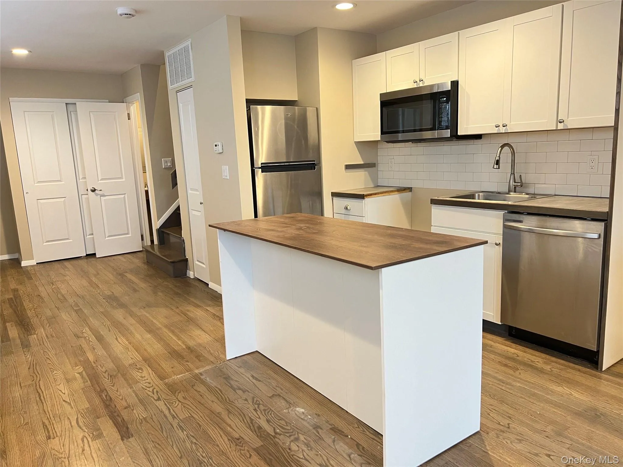 Kitchen with white cabinetry, appliances with stainless steel finishes, a center island, dark wood-style flooring, and recessed lighting Kitchen with white cabinetry, appliances with stainless steel finishes, a center island, dark wood-style flooring, and recessed lighting