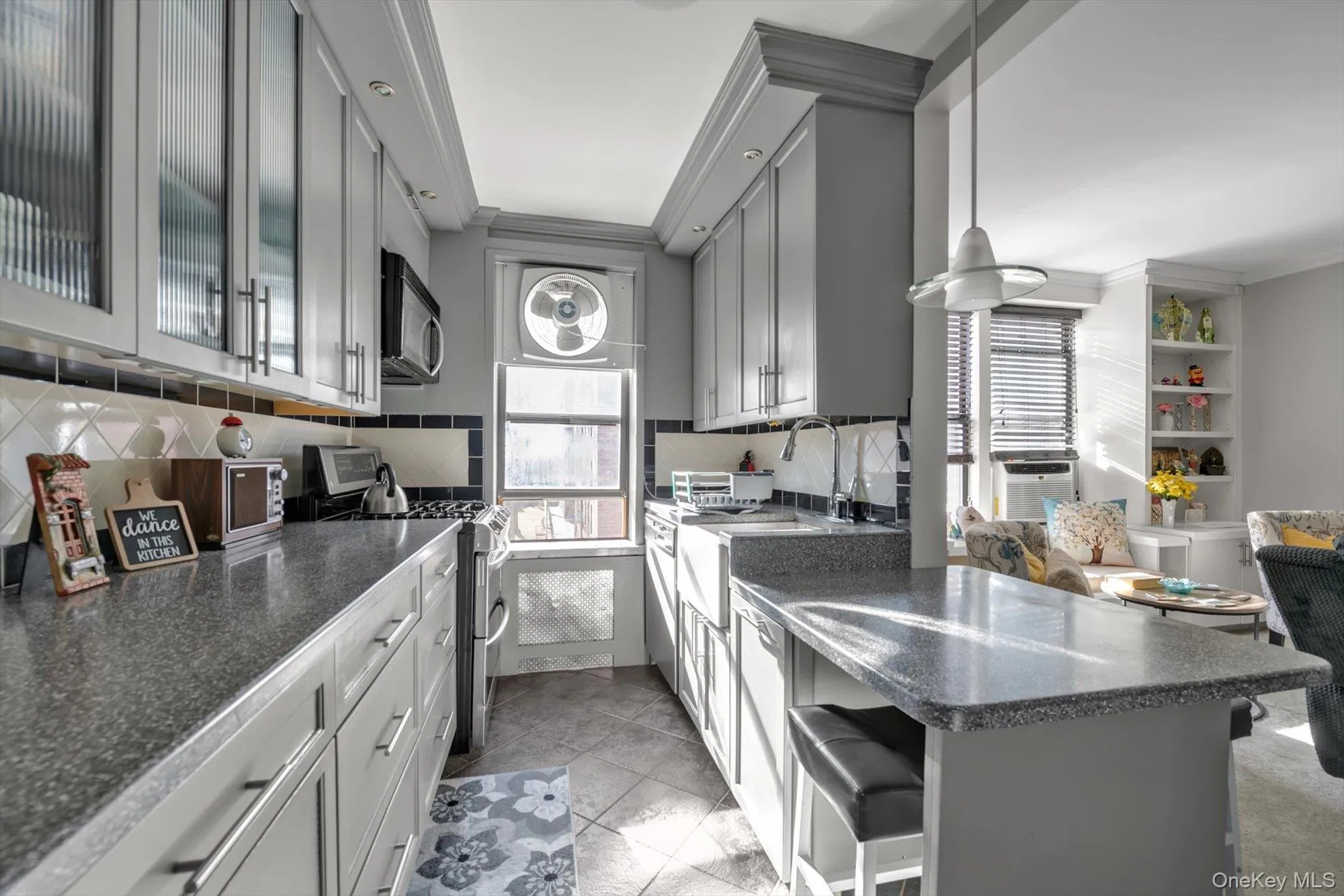 Kitchen featuring stainless steel range with gas cooktop, a breakfast bar, a peninsula, hanging light fixtures, and gray cabinetry Kitchen featuring stainless steel range with gas cooktop, a breakfast bar, a peninsula, hanging light fixtures, and gray cabinetry