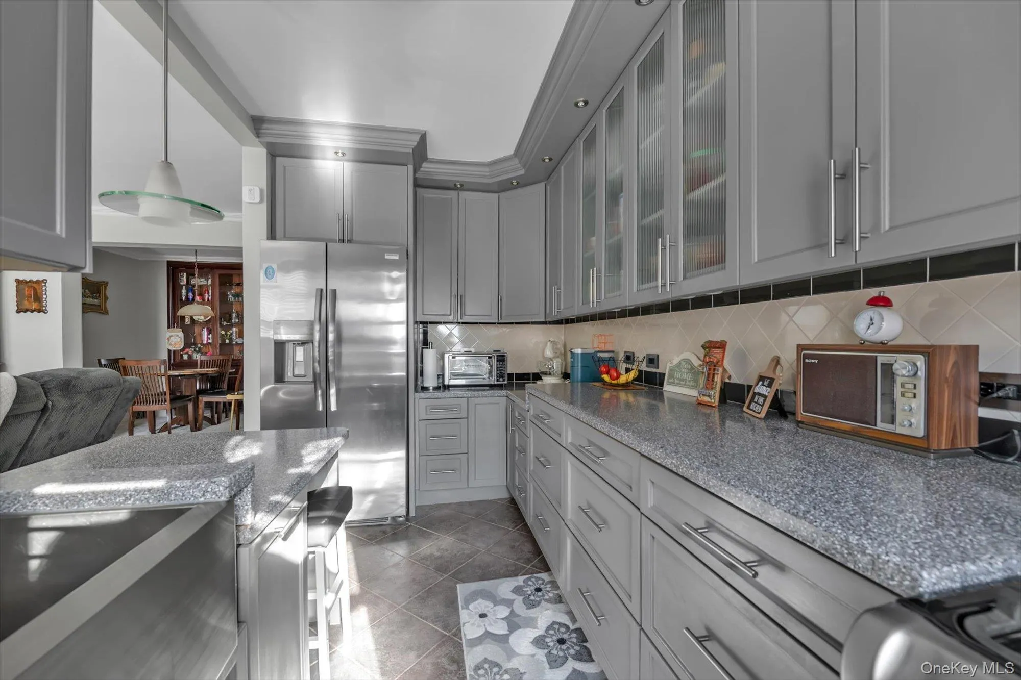 Kitchen featuring gray cabinets, stainless steel refrigerator with ice dispenser, glass insert cabinets, dark stone countertops, and decorative backsplash Kitchen featuring gray cabinets, stainless steel refrigerator with ice dispenser, glass insert cabinets, dark stone countertops, and decorative backsplash