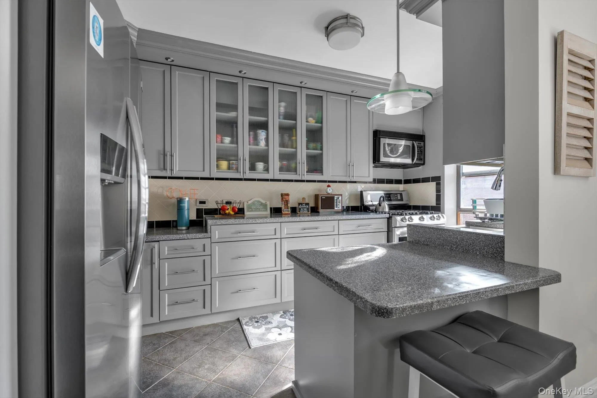 Kitchen with stainless steel appliances, gray cabinets, dark stone counters, a kitchen bar, and decorative light fixtures Kitchen with stainless steel appliances, gray cabinets, dark stone counters, a kitchen bar, and decorative light fixtures