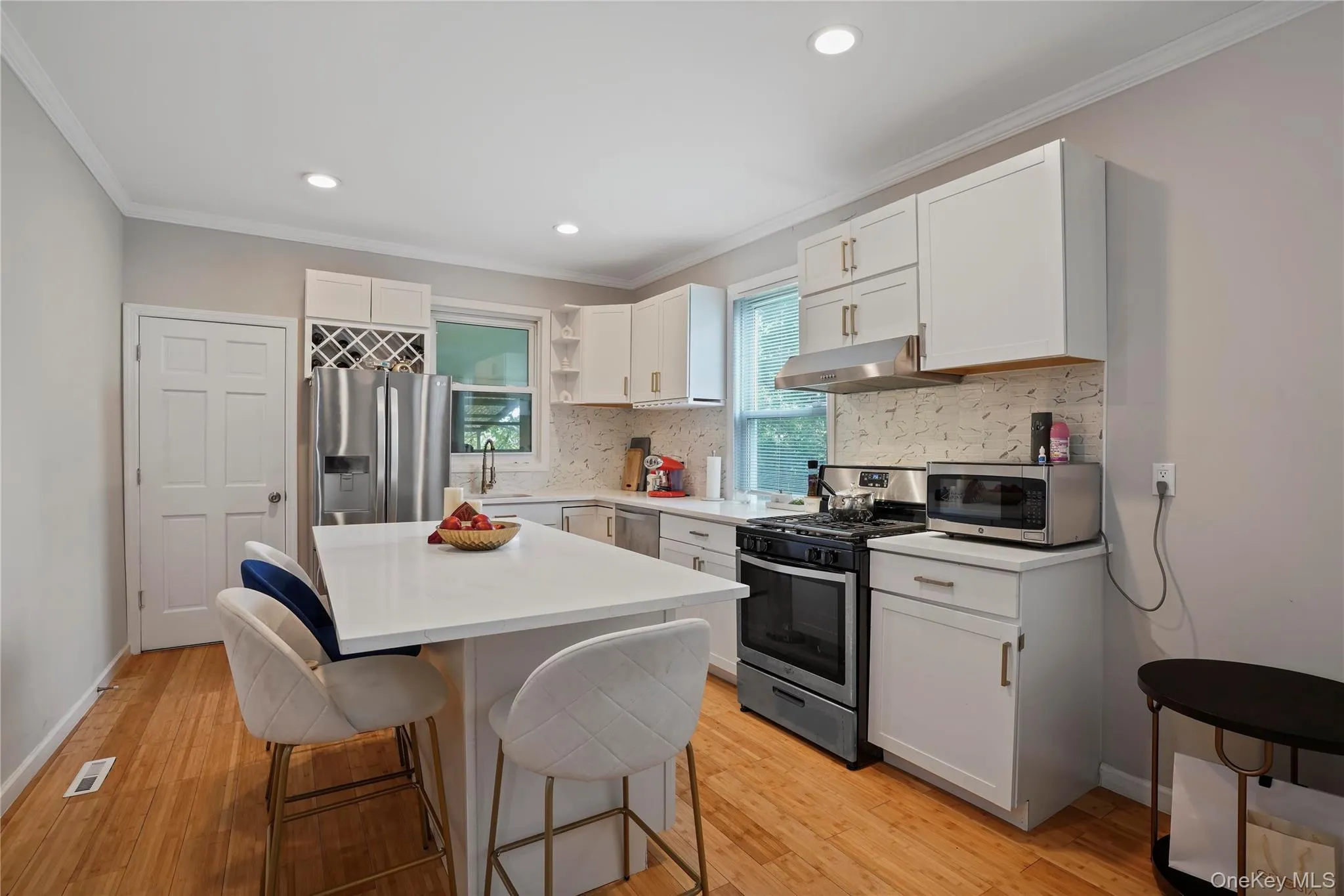 Kitchen with appliances with stainless steel finishes, white cabinetry, open shelves, a breakfast bar area, and a kitchen island Kitchen with appliances with stainless steel finishes, white cabinetry, open shelves, a breakfast bar area, and a kitchen island