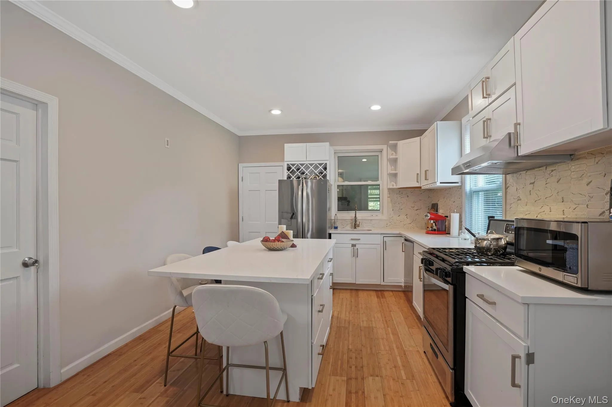 Kitchen with stainless steel appliances, white cabinetry, a kitchen bar, light wood-style flooring, and crown molding Kitchen with stainless steel appliances, white cabinetry, a kitchen bar, light wood-style flooring, and crown molding