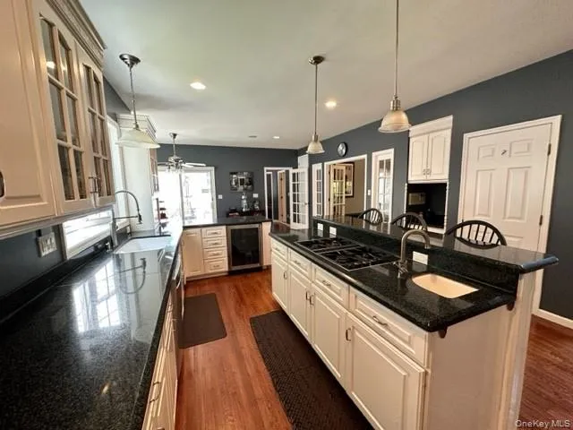 Kitchen with beverage cooler, dark stone counters, a kitchen bar, black gas stovetop, and dark wood finished floors Kitchen with beverage cooler, dark stone counters, a kitchen bar, black gas stovetop, and dark wood finished floors