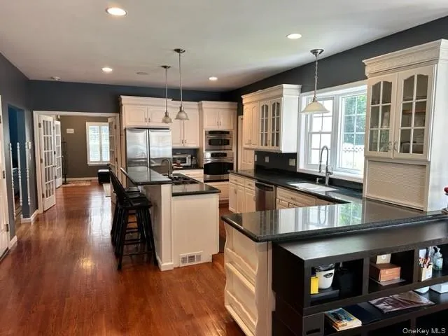 Kitchen featuring a breakfast bar area, glass insert cabinets, stainless steel appliances, a kitchen island with sink, and dark wood-style floors Kitchen featuring a breakfast bar area, glass insert cabinets, stainless steel appliances, a kitchen island with sink, and dark wood-style floors