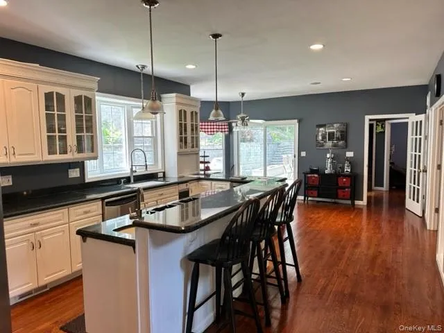 Kitchen with glass insert cabinets, a kitchen bar, recessed lighting, dark stone countertops, and hanging light fixtures Kitchen with glass insert cabinets, a kitchen bar, recessed lighting, dark stone countertops, and hanging light fixtures