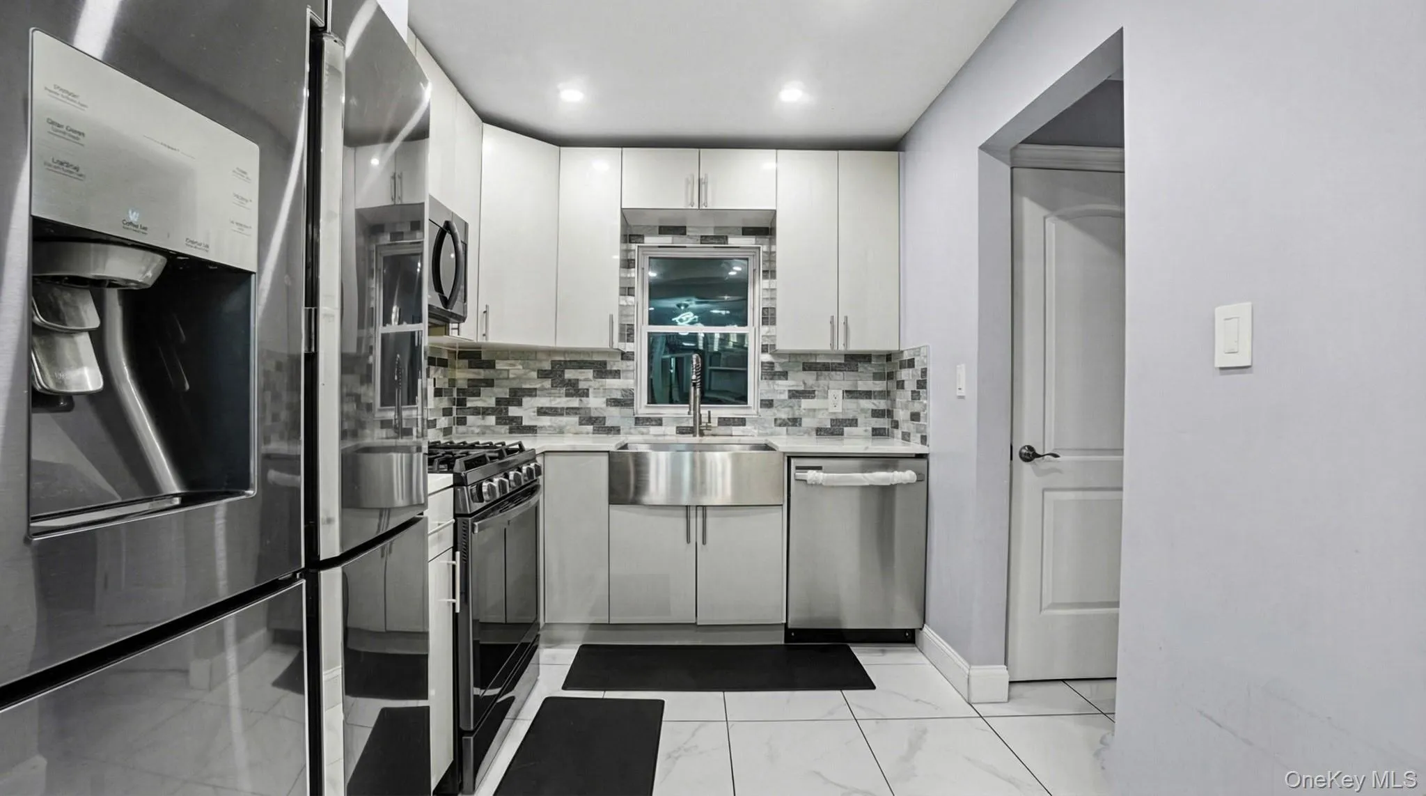 Kitchen featuring stainless steel appliances, decorative backsplash, light stone countertops, white cabinets, and light marble finish flooring Kitchen featuring stainless steel appliances, decorative backsplash, light stone countertops, white cabinets, and light marble finish flooring
