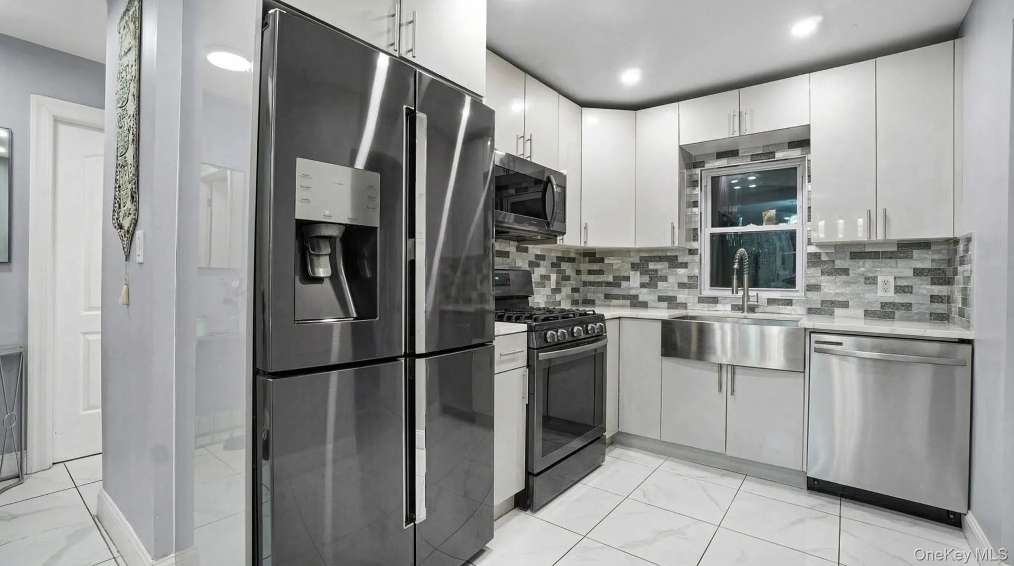 Kitchen featuring appliances with stainless steel finishes, light marble finish flooring, tasteful backsplash, light stone counters, and white cabinetry Kitchen featuring appliances with stainless steel finishes, light marble finish flooring, tasteful backsplash, light stone counters, and white cabinetry