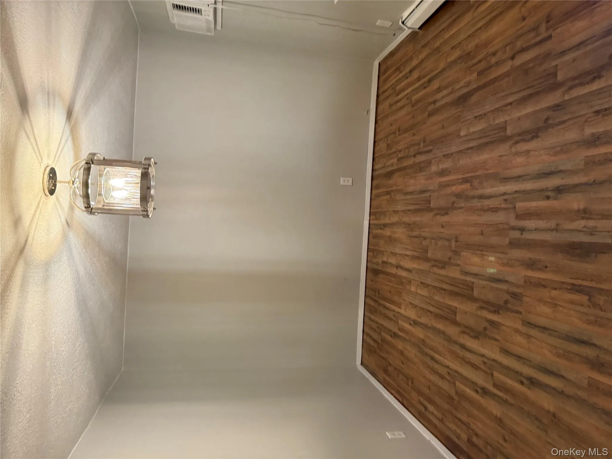 Spare room featuring dark wood finished floors, a textured ceiling, a baseboard heating unit, a chandelier, and a wall mounted air conditioner Spare room featuring dark wood finished floors, a textured ceiling, a baseboard heating unit, a chandelier, and a wall mounted air conditioner