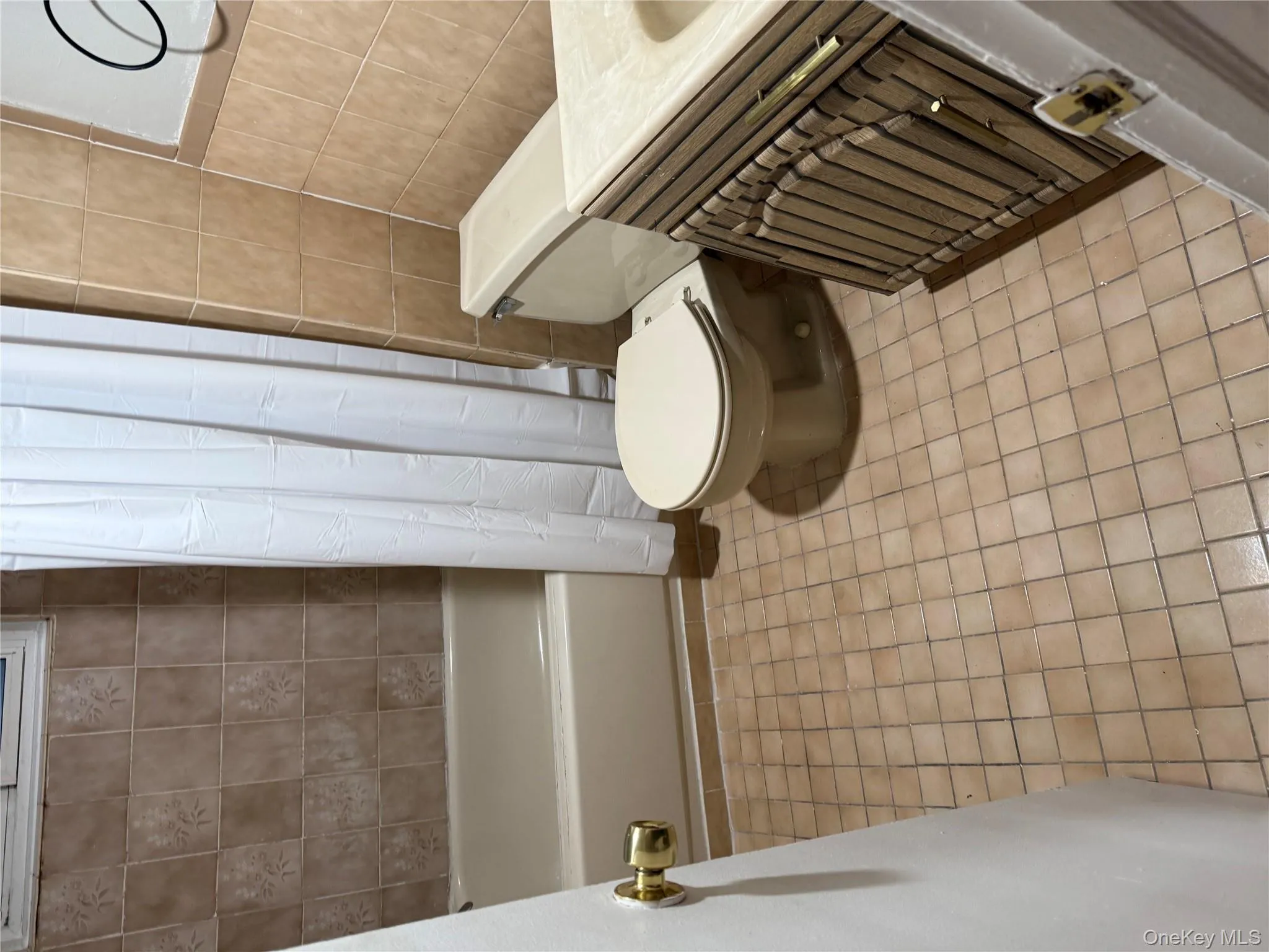 Bathroom featuring vanity, shower / bath combo with shower curtain, tile walls, and light tile patterned floors Bathroom featuring vanity, shower / bath combo with shower curtain, tile walls, and light tile patterned floors