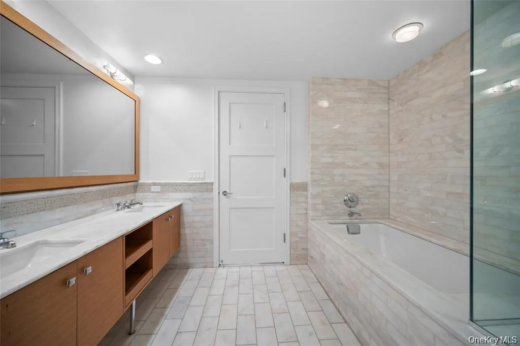 Bathroom featuring tile walls, double vanity, tiled bath, a wainscoted wall, and recessed lighting Bathroom featuring tile walls, double vanity, tiled bath, a wainscoted wall, and recessed lighting