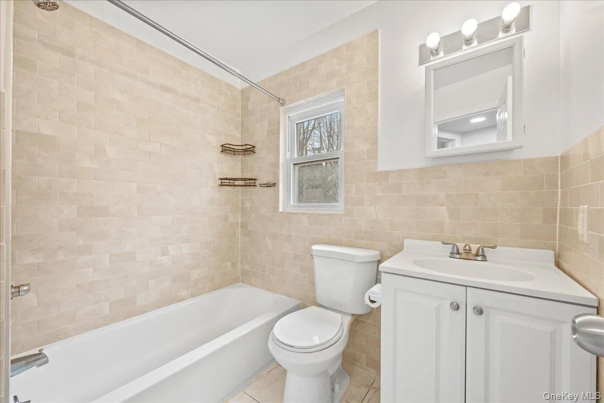 Full bathroom featuring bathtub / shower combination, vanity, tile walls, and light tile patterned floors Full bathroom featuring bathtub / shower combination, vanity, tile walls, and light tile patterned floors