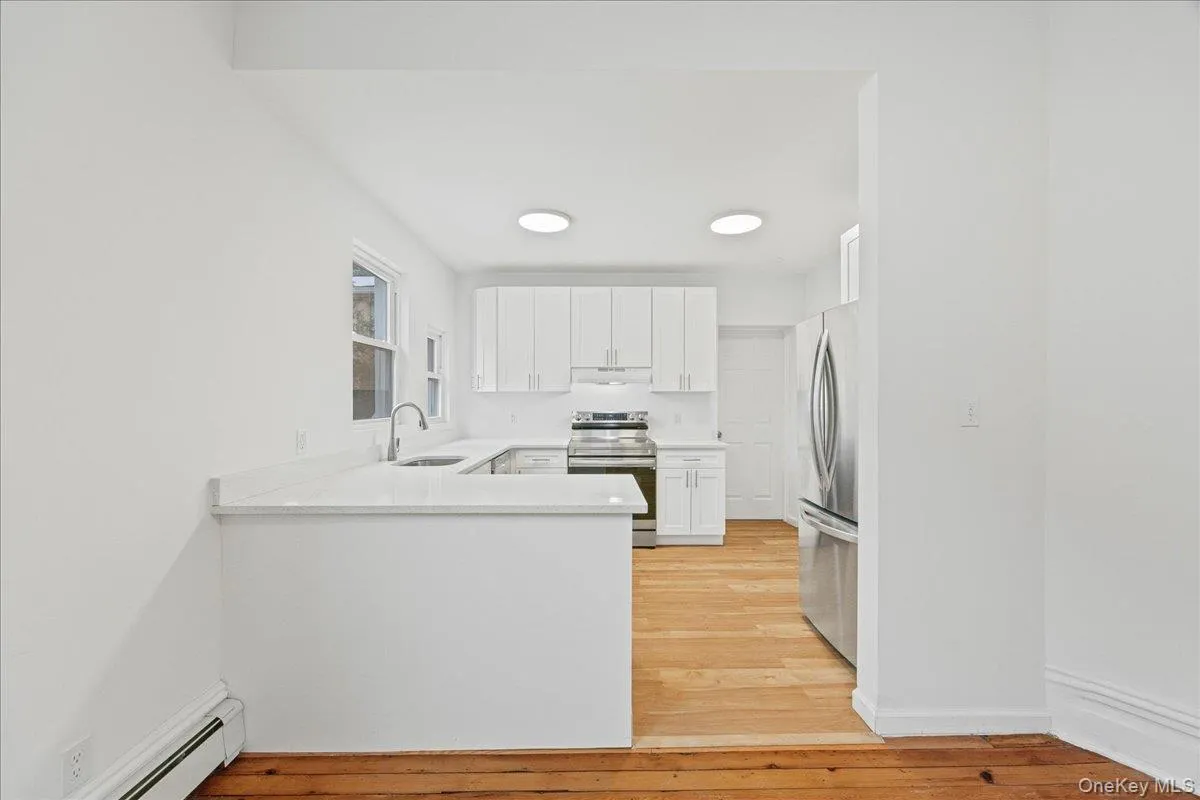 Kitchen featuring white cabinets, appliances with stainless steel finishes, baseboard heating, a peninsula, and light wood-style flooring Kitchen featuring white cabinets, appliances with stainless steel finishes, baseboard heating, a peninsula, and light wood-style flooring