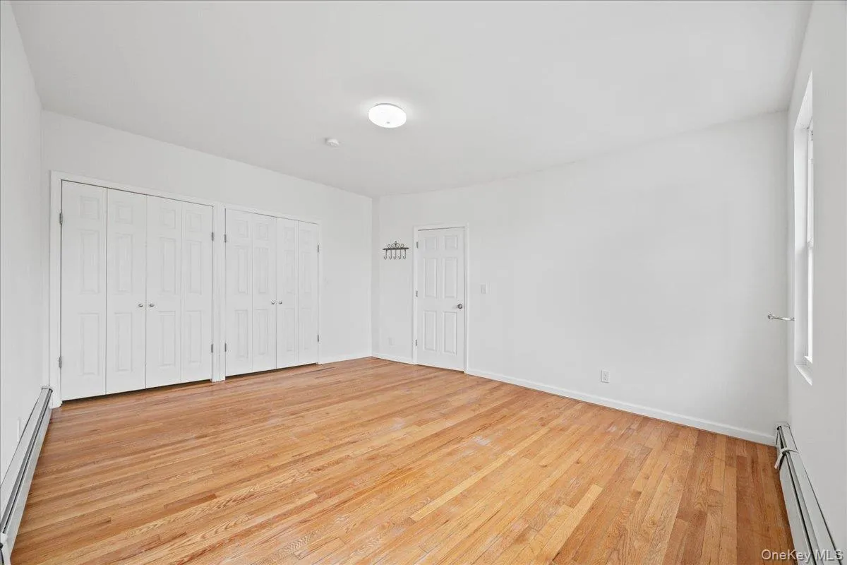 Unfurnished bedroom with baseboard heating, multiple closets, and light wood-style flooring Unfurnished bedroom with baseboard heating, multiple closets, and light wood-style flooring