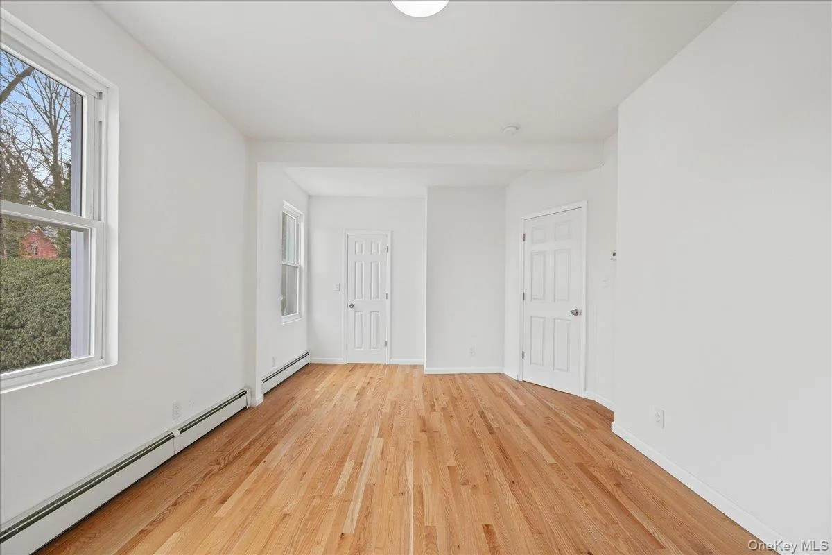 Unfurnished bedroom featuring a baseboard heating unit, light wood-style floors, and multiple windows Unfurnished bedroom featuring a baseboard heating unit, light wood-style floors, and multiple windows