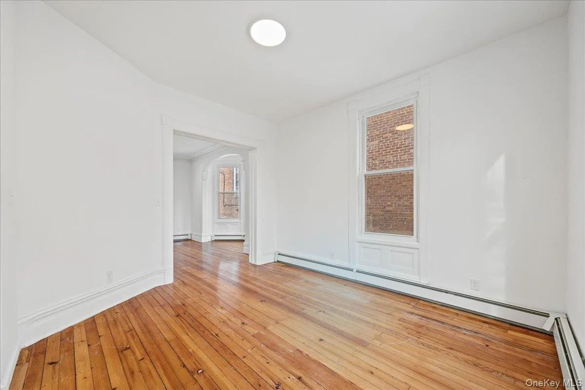 Spare room featuring light wood finished floors, a baseboard radiator, arched walkways, and a baseboard heating unit Spare room featuring light wood finished floors, a baseboard radiator, arched walkways, and a baseboard heating unit