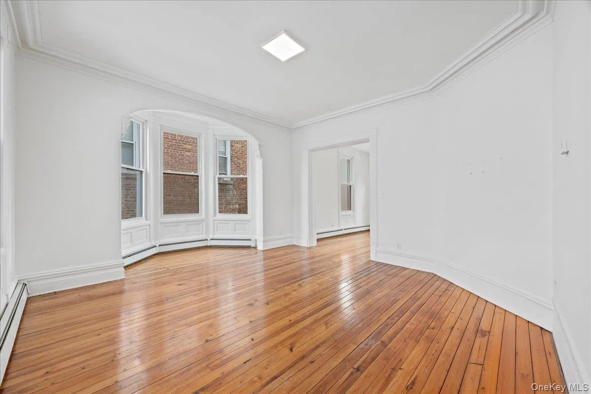 Empty room with baseboard heating, light wood finished floors, and ornamental molding Empty room with baseboard heating, light wood finished floors, and ornamental molding