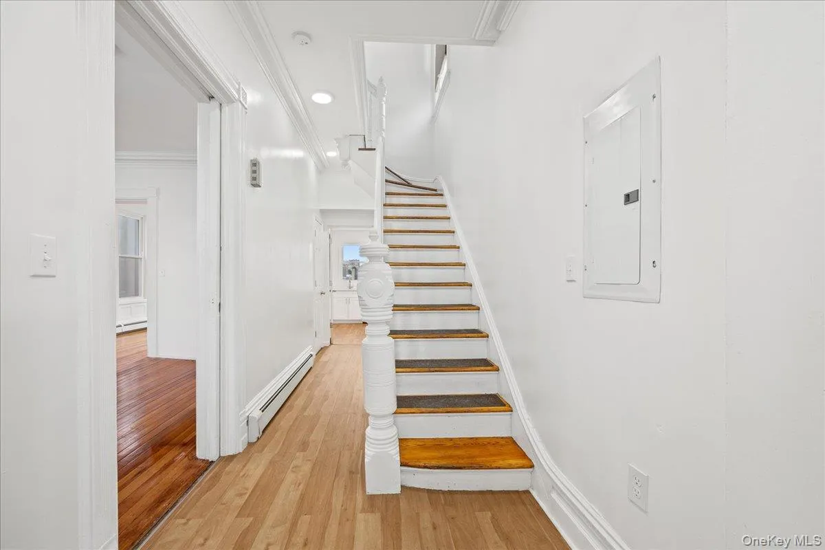 Stairs with a baseboard radiator, wood finished floors, electric panel, crown molding, and recessed lighting Stairs with a baseboard radiator, wood finished floors, electric panel, crown molding, and recessed lighting