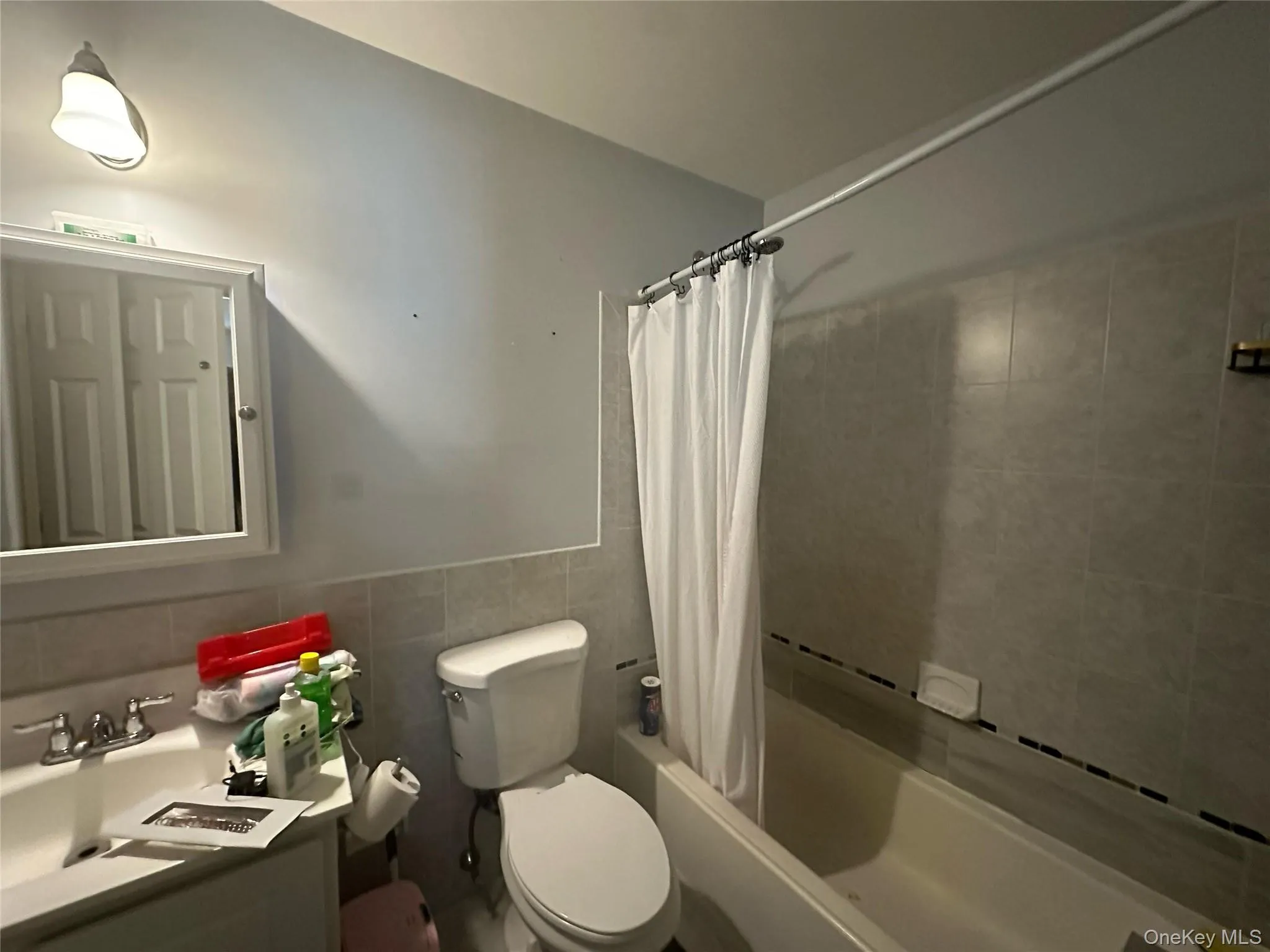 Bathroom with shower / tub combo with curtain, vanity, tile walls, and a wainscoted wall Bathroom with shower / tub combo with curtain, vanity, tile walls, and a wainscoted wall