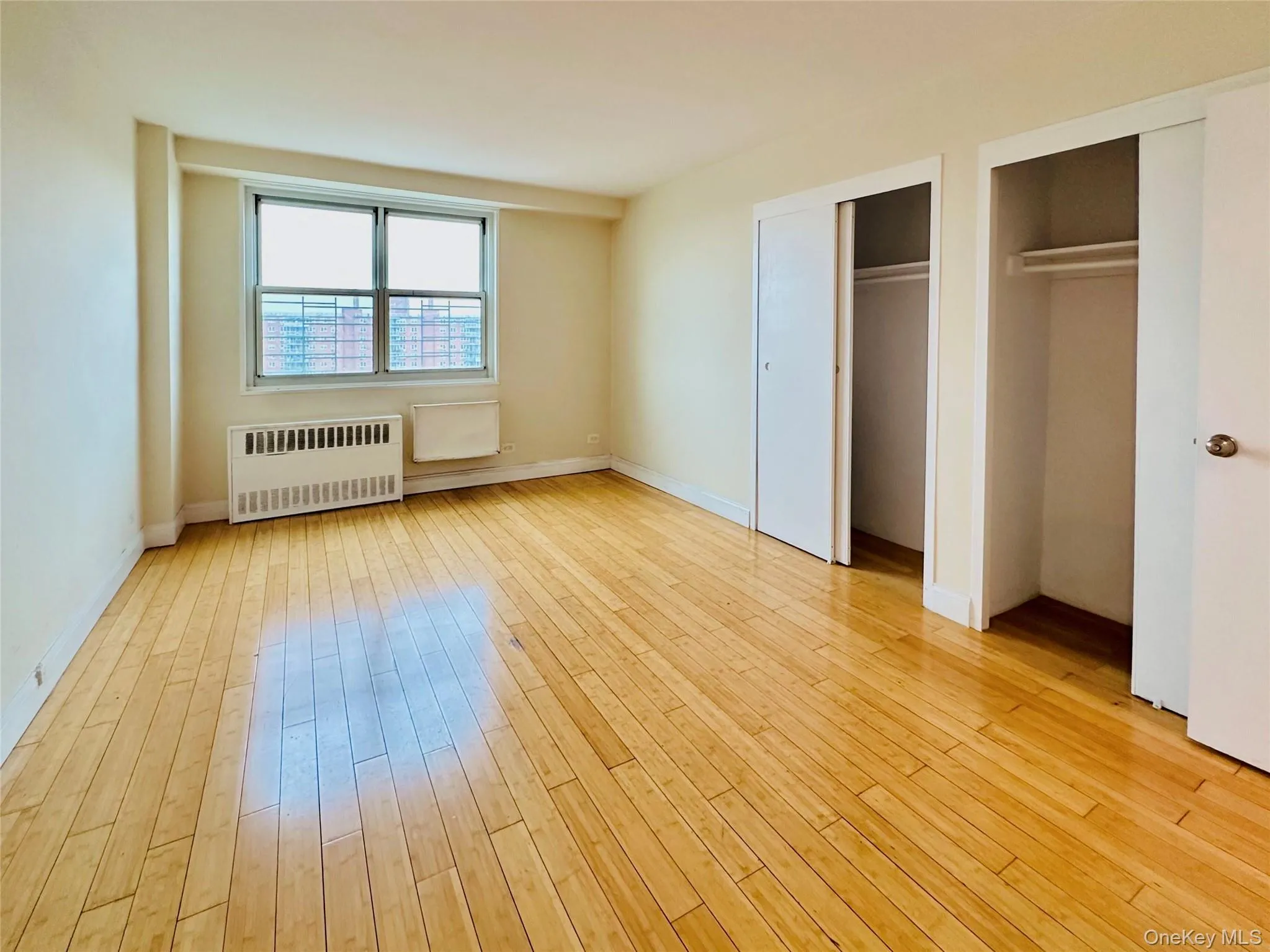 Unfurnished bedroom featuring radiator, multiple closets, and light wood-style floors Unfurnished bedroom featuring radiator, multiple closets, and light wood-style floors