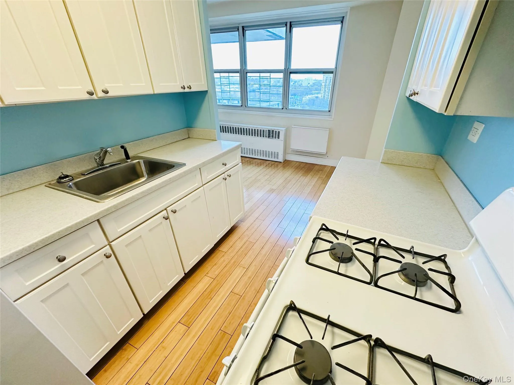 Kitchen featuring white cabinets, radiator heating unit, light wood finished floors, and white range with gas cooktop Kitchen featuring white cabinets, radiator heating unit, light wood finished floors, and white range with gas cooktop