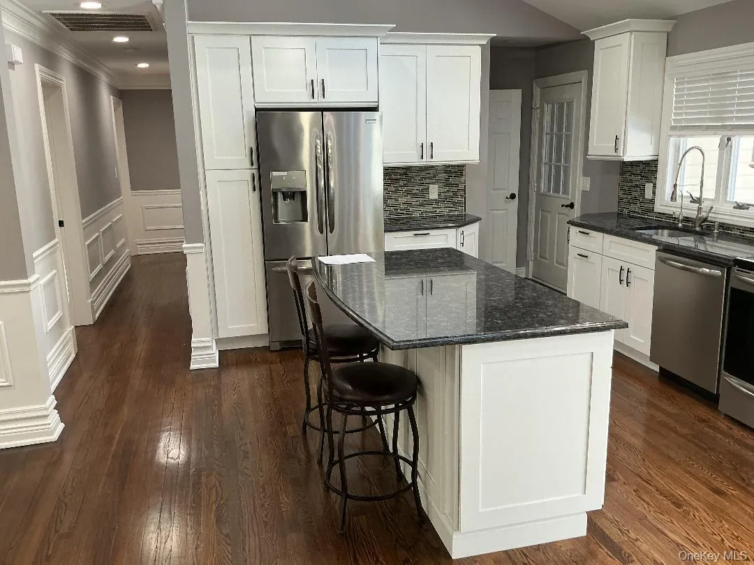 Kitchen featuring dark stone counters, appliances with stainless steel finishes, white cabinetry, tasteful backsplash, and dark wood finished floors Kitchen featuring dark stone counters, appliances with stainless steel finishes, white cabinetry, tasteful backsplash, and dark wood finished floors