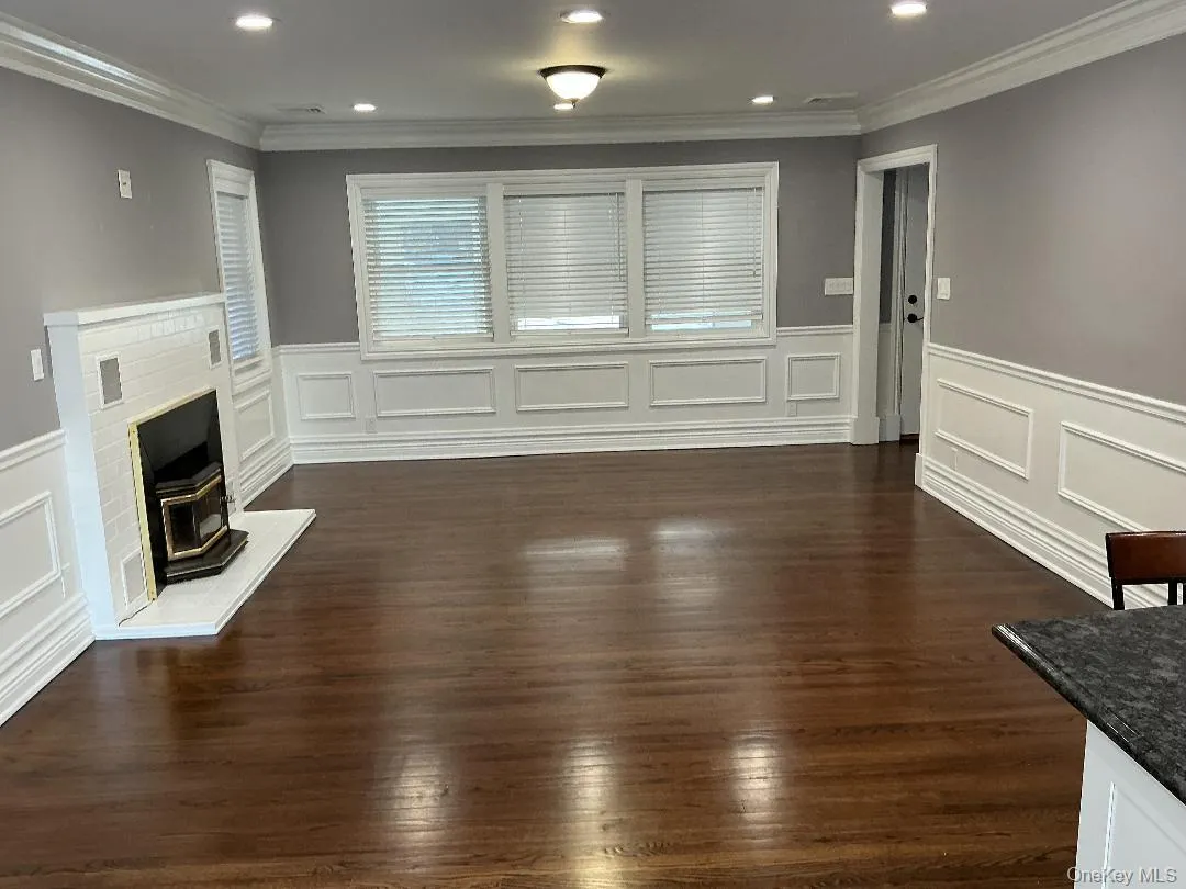 Unfurnished living room with dark wood finished floors, wainscoting, recessed lighting, ornamental molding, and a wood stove Unfurnished living room with dark wood finished floors, wainscoting, recessed lighting, ornamental molding, and a wood stove