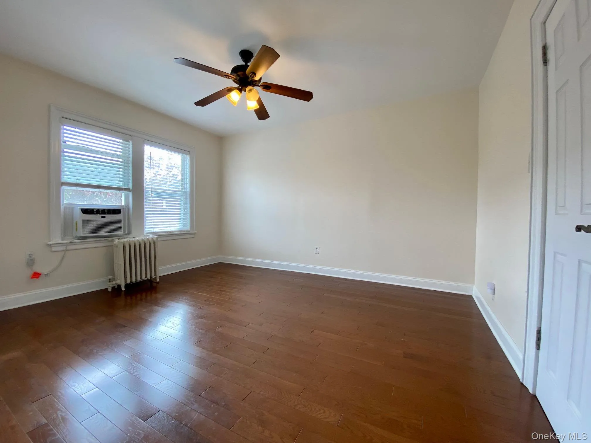 Spare room featuring dark wood-style floors, radiator, a ceiling fan, and cooling unit Spare room featuring dark wood-style floors, radiator, a ceiling fan, and cooling unit