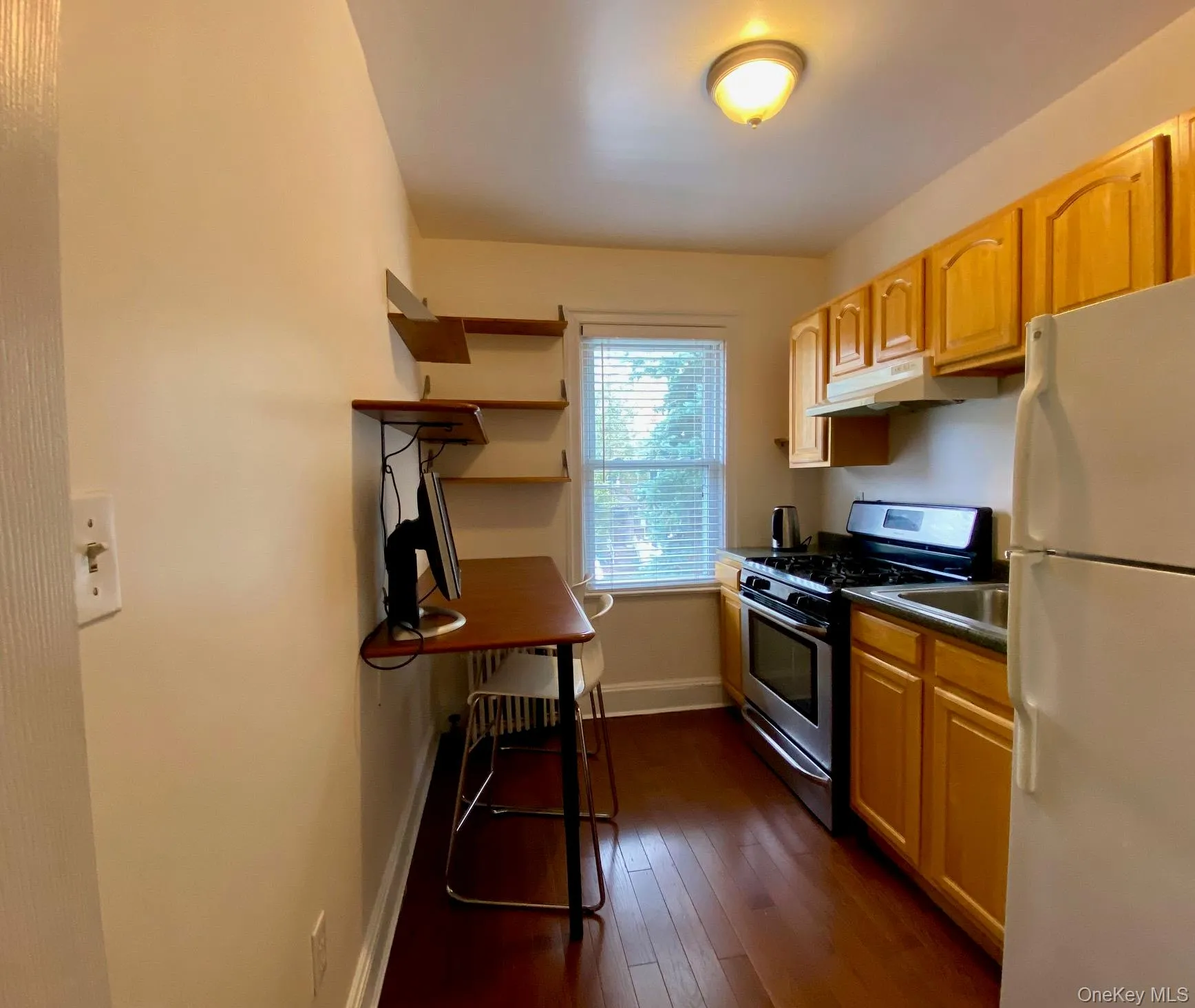 Kitchen with dark countertops, stainless steel gas range, freestanding refrigerator, dark wood-type flooring, and light brown cabinets Kitchen with dark countertops, stainless steel gas range, freestanding refrigerator, dark wood-type flooring, and light brown cabinets