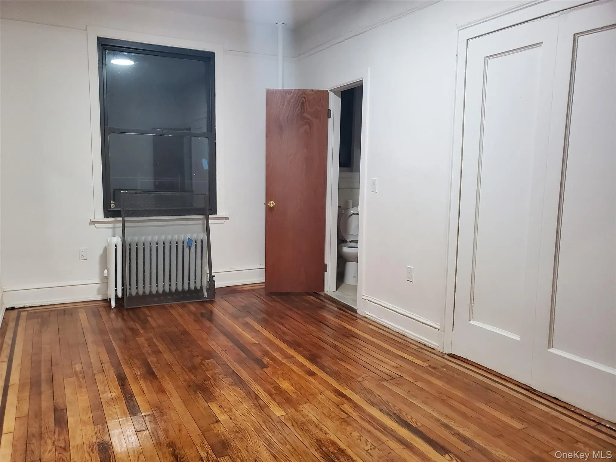 Unfurnished bedroom featuring radiator, hardwood / wood-style floors, and connected bathroom Unfurnished bedroom featuring radiator, hardwood / wood-style floors, and connected bathroom
