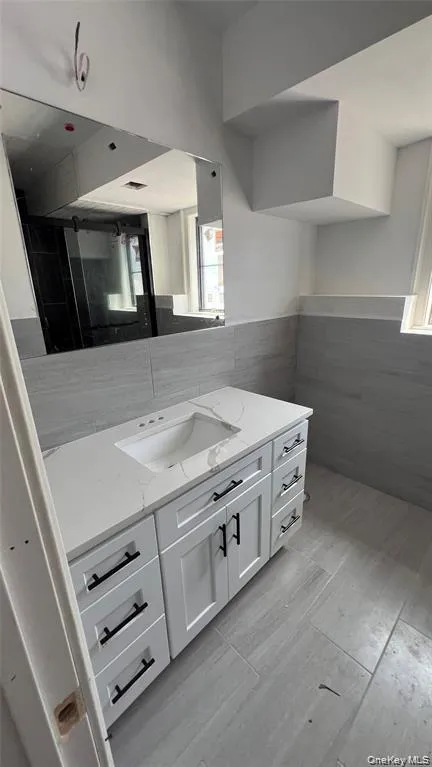 Bathroom featuring vanity, tile walls, wainscoting, and light wood finished floors Bathroom featuring vanity, tile walls, wainscoting, and light wood finished floors