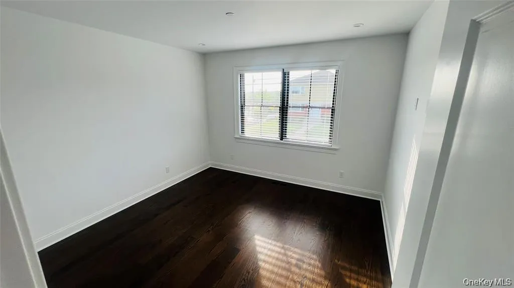Empty room with dark wood-style flooring and baseboards Empty room with dark wood-style flooring and baseboards