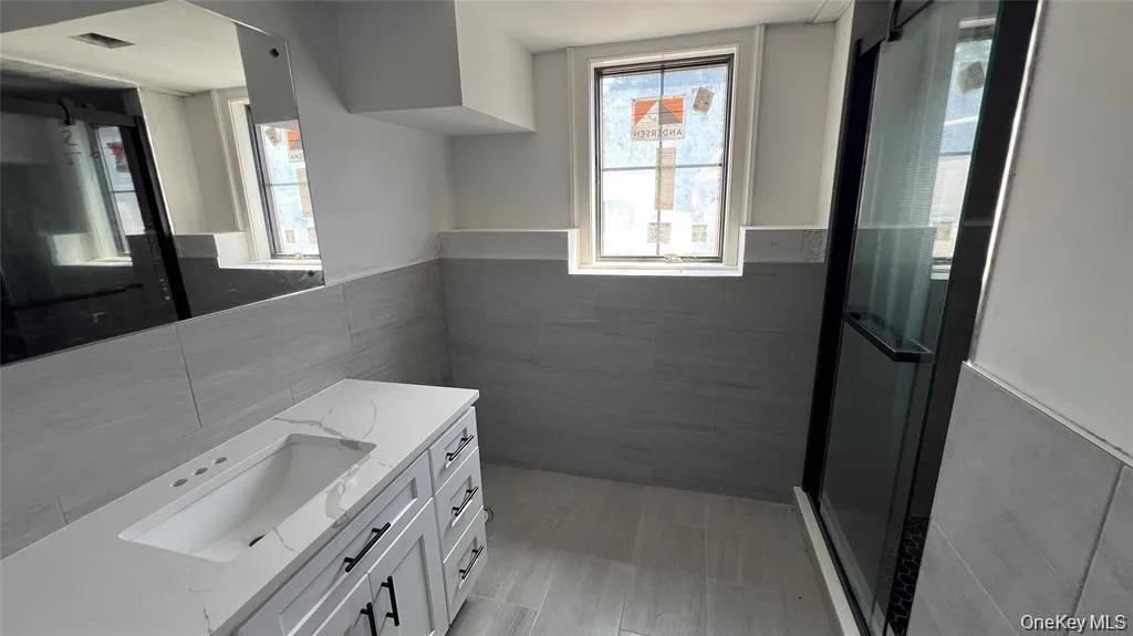 Bathroom with a wainscoted wall, tile walls, vanity, a shower stall, and plenty of natural light Bathroom with a wainscoted wall, tile walls, vanity, a shower stall, and plenty of natural light