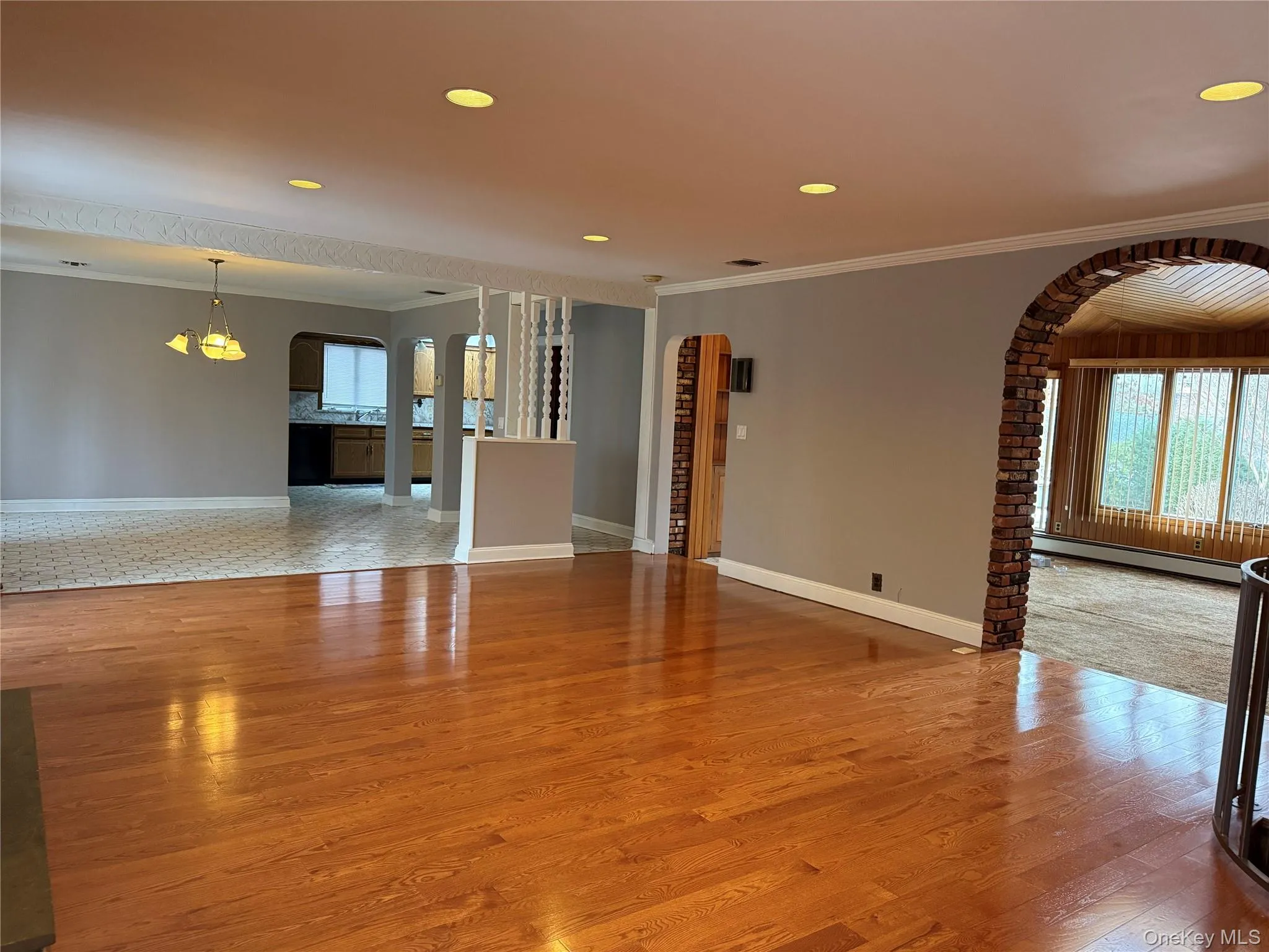 Unfurnished living room featuring arched walkways, crown molding, light wood finished floors, recessed lighting, and a baseboard radiator Unfurnished living room featuring arched walkways, crown molding, light wood finished floors, recessed lighting, and a baseboard radiator