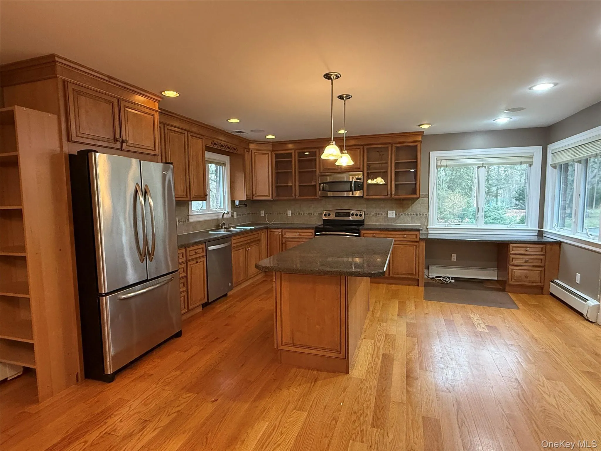 Kitchen with appliances with stainless steel finishes, brown cabinetry, decorative light fixtures, a center island, and dark stone counters Kitchen with appliances with stainless steel finishes, brown cabinetry, decorative light fixtures, a center island, and dark stone counters