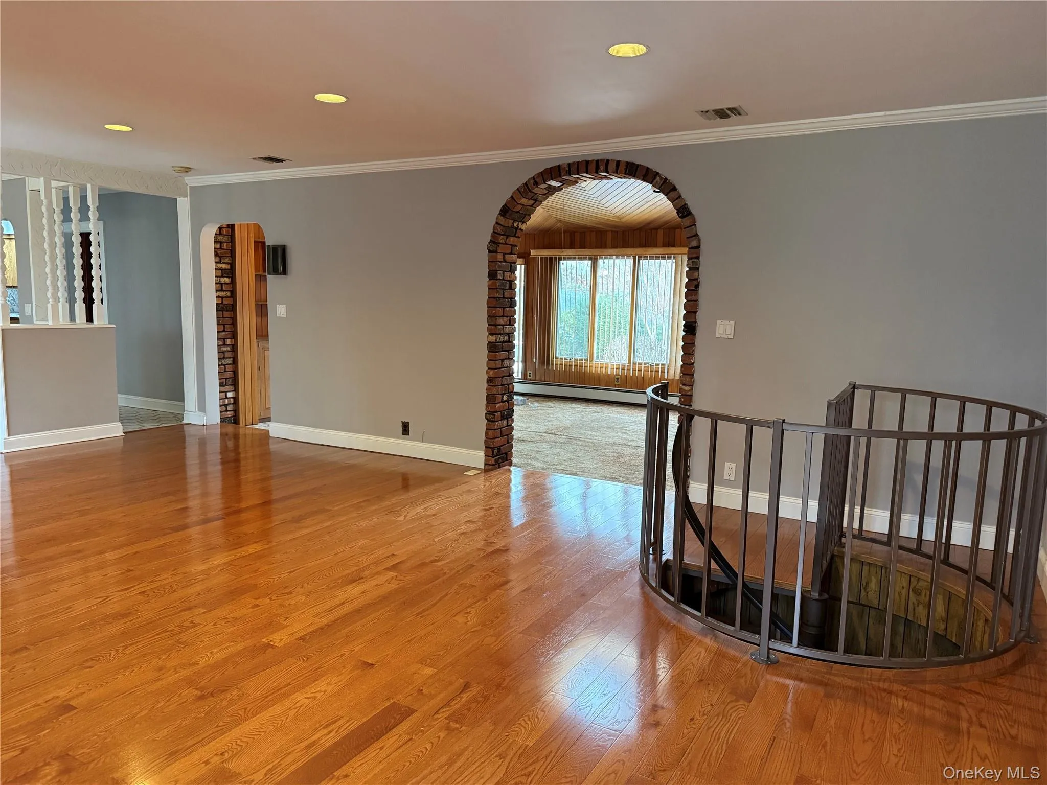 Empty room with arched walkways, light wood-style flooring, a baseboard heating unit, recessed lighting, and ornamental molding Empty room with arched walkways, light wood-style flooring, a baseboard heating unit, recessed lighting, and ornamental molding