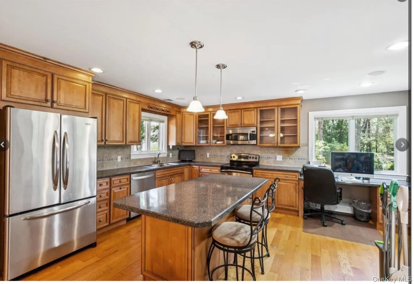 Kitchen featuring brown cabinetry, stainless steel appliances, dark stone counters, hanging light fixtures, and recessed lighting Kitchen featuring brown cabinetry, stainless steel appliances, dark stone counters, hanging light fixtures, and recessed lighting
