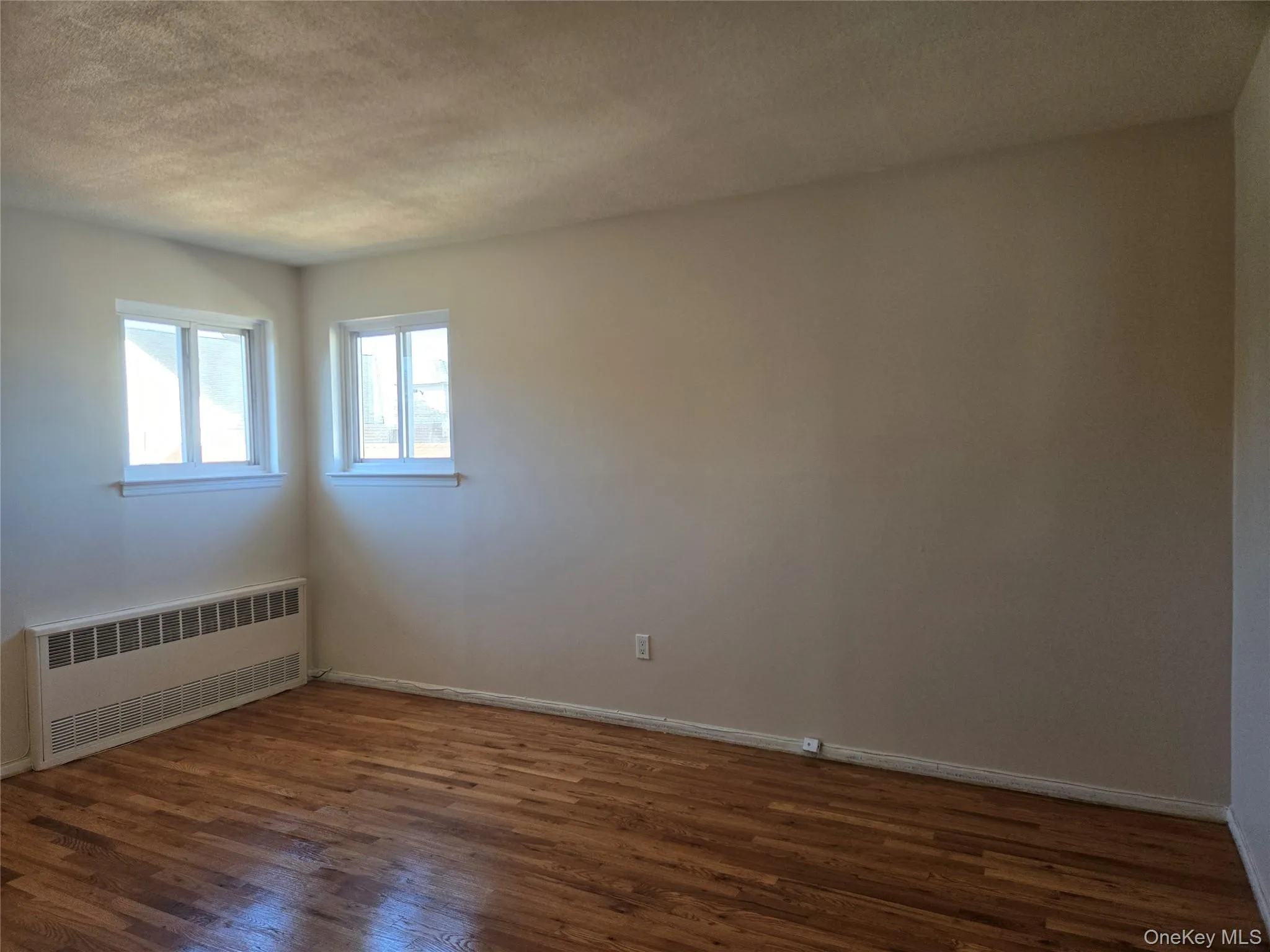 Unfurnished room with radiator heating unit, a textured ceiling, and dark wood-type flooring Unfurnished room with radiator heating unit, a textured ceiling, and dark wood-type flooring