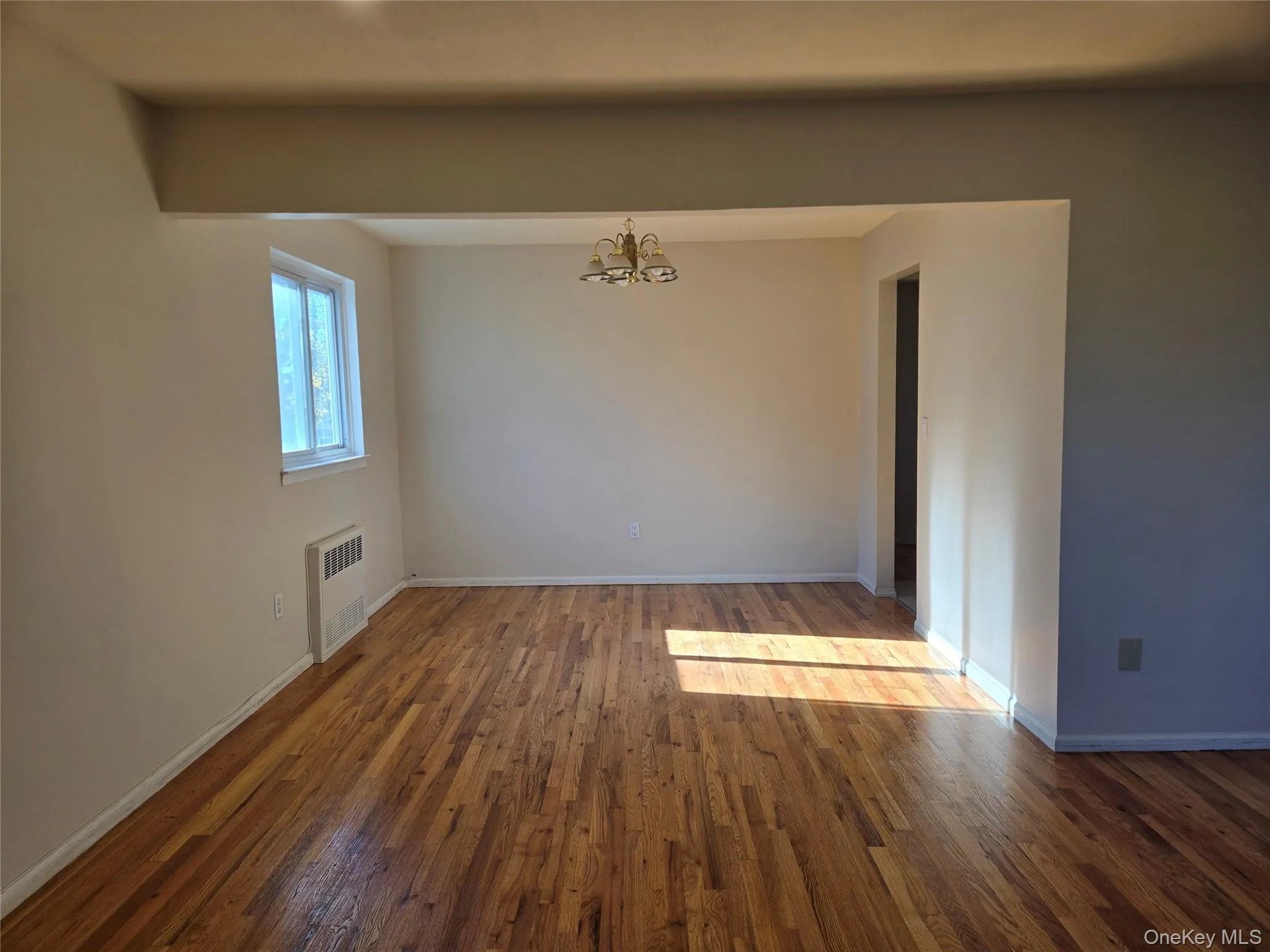 Spare room with a chandelier, dark wood-style flooring, and radiator Spare room with a chandelier, dark wood-style flooring, and radiator