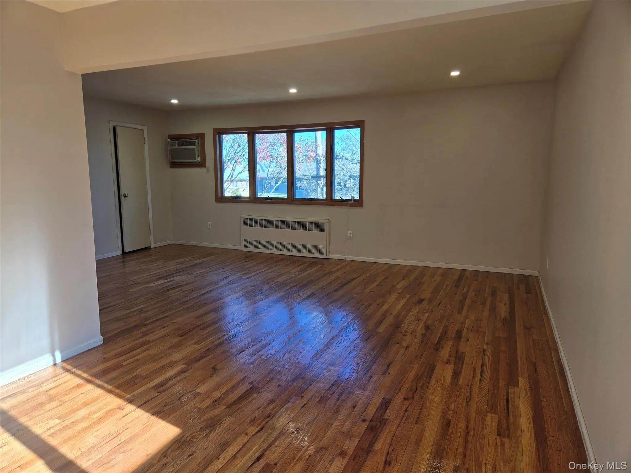 Empty room with dark wood finished floors, radiator, recessed lighting, and a wall mounted AC Empty room with dark wood finished floors, radiator, recessed lighting, and a wall mounted AC