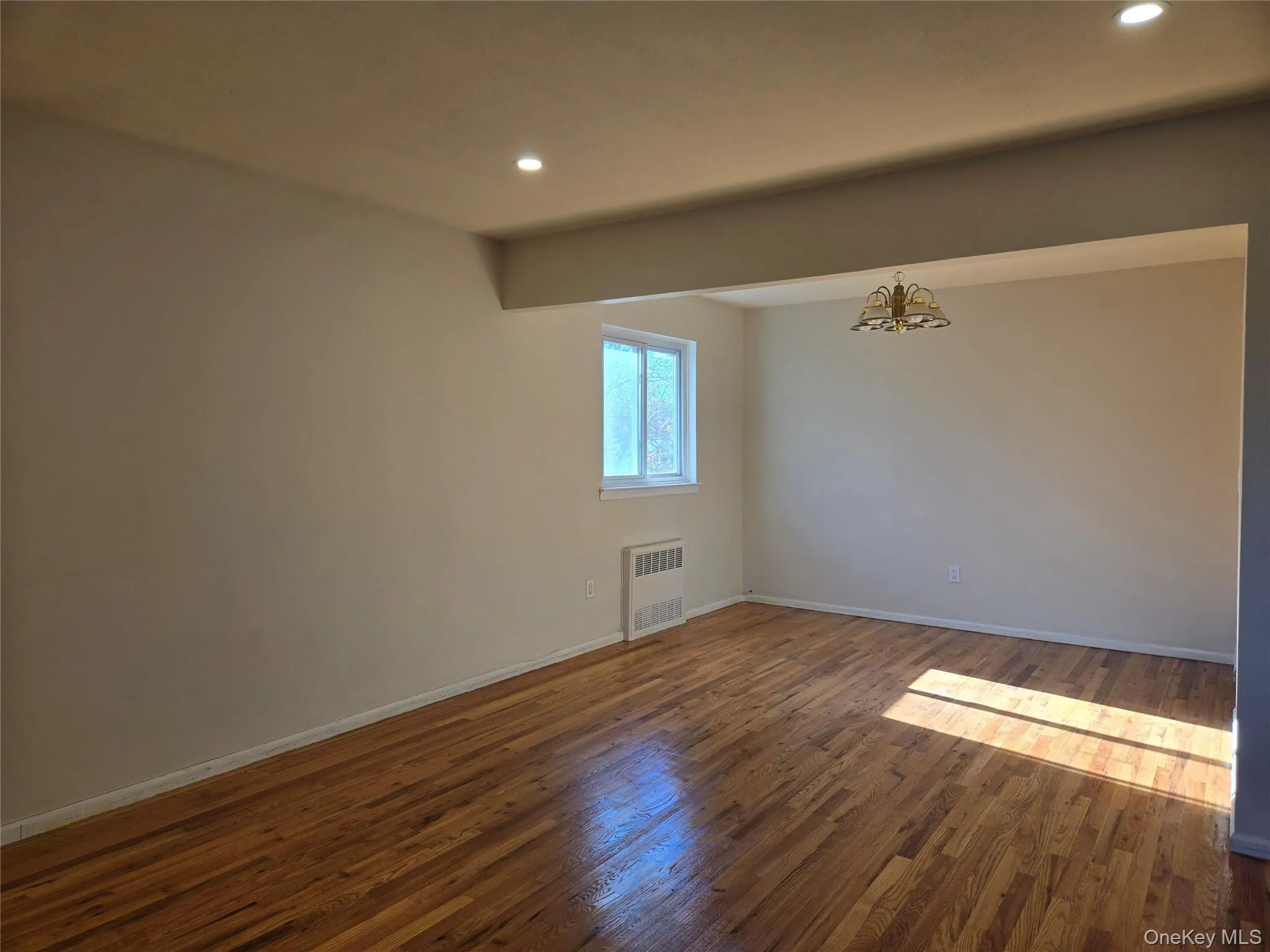 Spare room with dark wood finished floors, recessed lighting, a chandelier, and radiator heating unit Spare room with dark wood finished floors, recessed lighting, a chandelier, and radiator heating unit