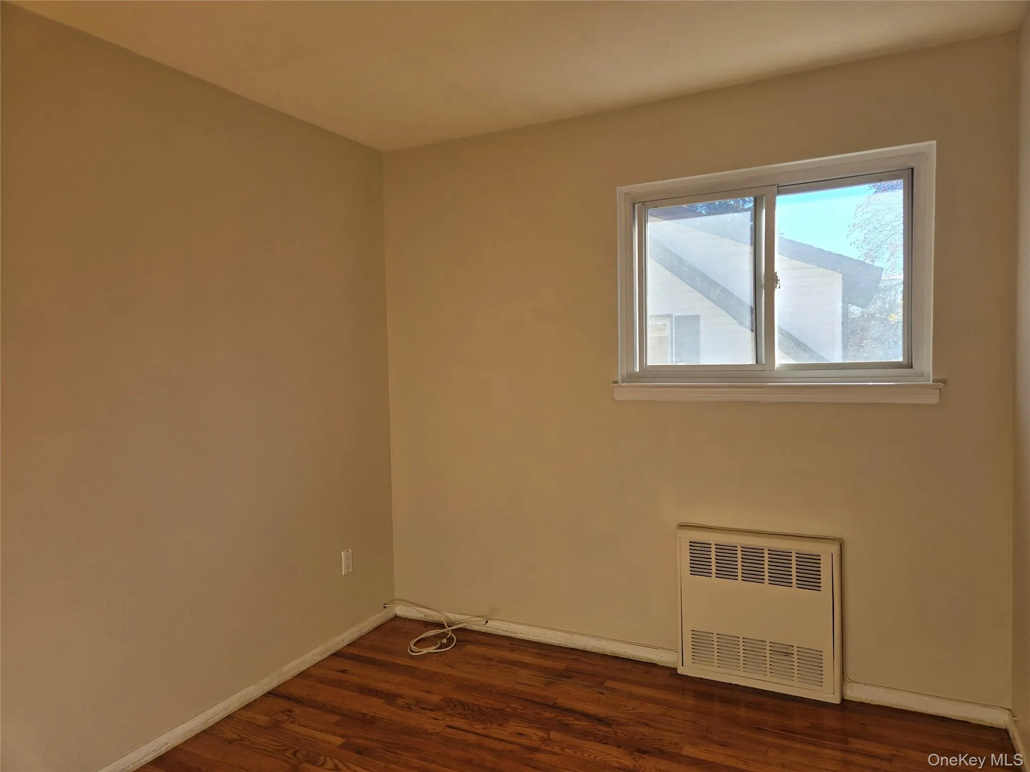 Unfurnished room featuring radiator heating unit and dark wood finished floors Unfurnished room featuring radiator heating unit and dark wood finished floors
