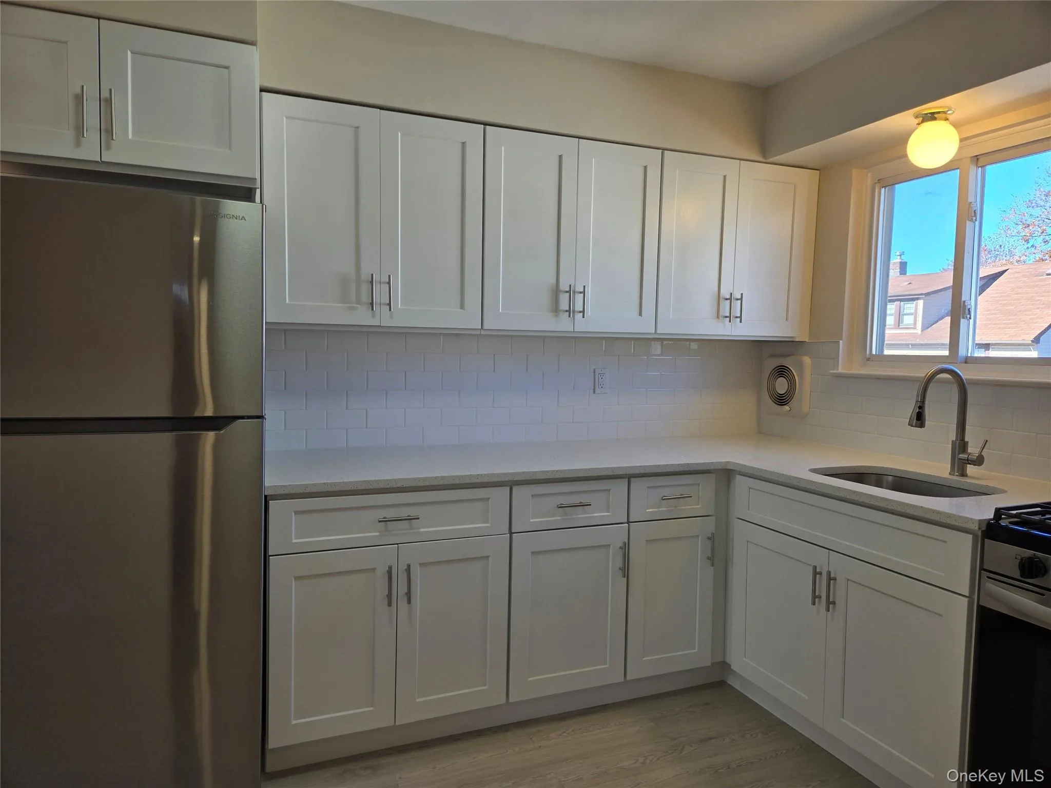 Kitchen with white cabinets, freestanding refrigerator, light stone countertops, and backsplash Kitchen with white cabinets, freestanding refrigerator, light stone countertops, and backsplash