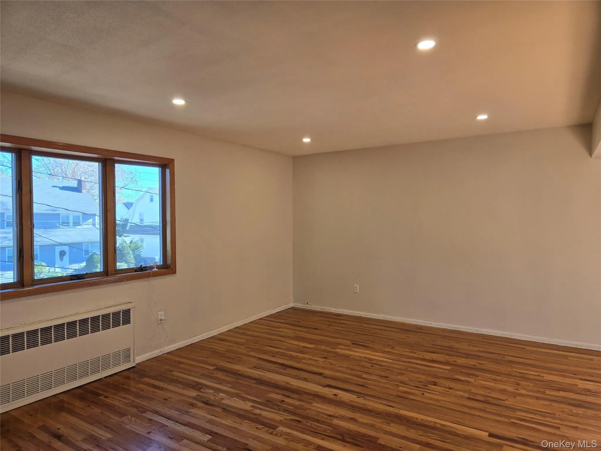 Empty room with radiator heating unit, recessed lighting, and dark wood-type flooring Empty room with radiator heating unit, recessed lighting, and dark wood-type flooring